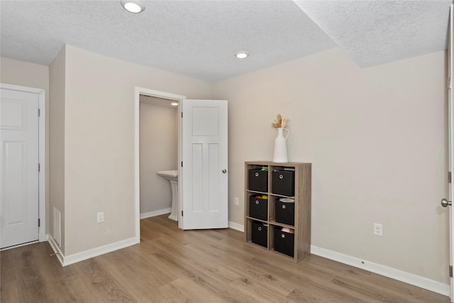 unfurnished bedroom with recessed lighting, wood finished floors, a textured ceiling, and baseboards