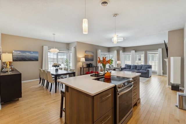 kitchen featuring hanging light fixtures, a kitchen island with sink, light wood-type flooring, and stainless steel electric range