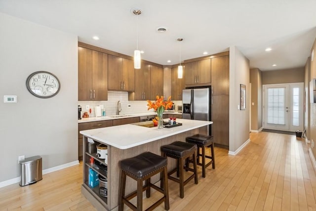 kitchen featuring pendant lighting, sink, light hardwood / wood-style flooring, a kitchen bar, and stainless steel fridge with ice dispenser