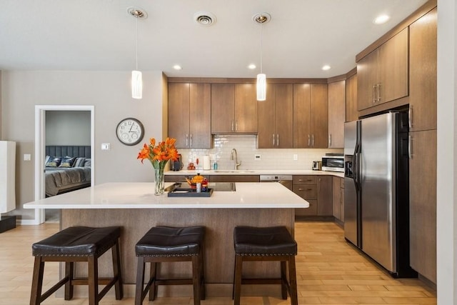 kitchen with pendant lighting, stainless steel appliances, light hardwood / wood-style floors, a kitchen bar, and decorative backsplash