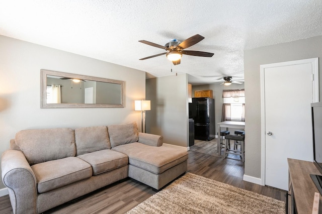 living area with baseboards, a ceiling fan, dark wood-style flooring, and a textured ceiling