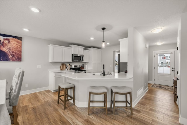 kitchen featuring white cabinetry, light wood-type flooring, stainless steel appliances, and a kitchen bar