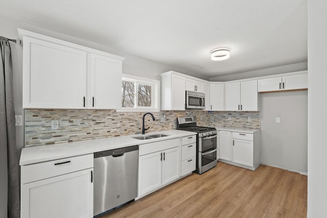 kitchen featuring appliances with stainless steel finishes, sink, white cabinets, backsplash, and light hardwood / wood-style flooring