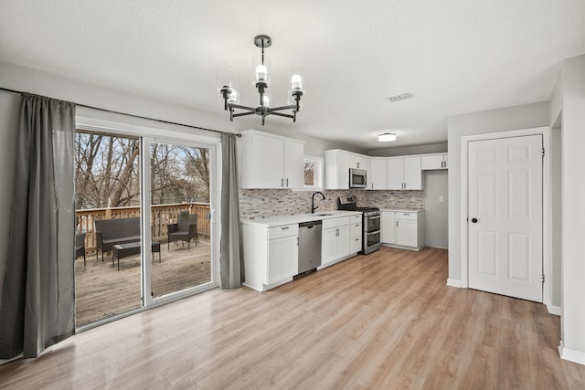 kitchen with hanging light fixtures, stainless steel appliances, tasteful backsplash, white cabinets, and light wood-type flooring