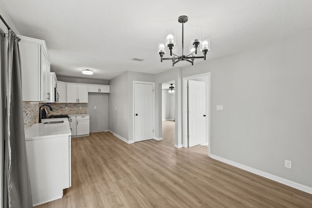 kitchen featuring light hardwood / wood-style flooring, white cabinets, pendant lighting, ceiling fan with notable chandelier, and backsplash