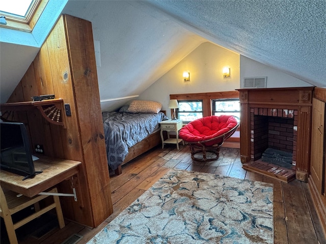 bedroom with hardwood / wood-style floors, lofted ceiling with skylight, a textured ceiling, and a brick fireplace