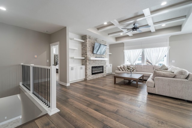 living room featuring dark wood-type flooring, coffered ceiling, beam ceiling, and a stone fireplace