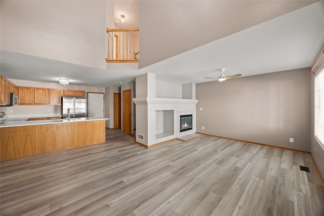 kitchen featuring light hardwood / wood-style flooring, appliances with stainless steel finishes, kitchen peninsula, a tile fireplace, and ceiling fan