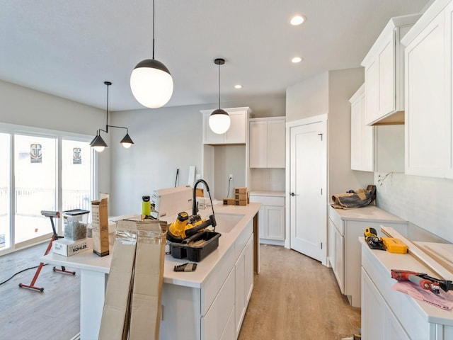 kitchen with pendant lighting, white cabinetry, sink, a kitchen island with sink, and light hardwood / wood-style flooring