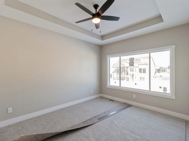 carpeted spare room with ceiling fan and a raised ceiling