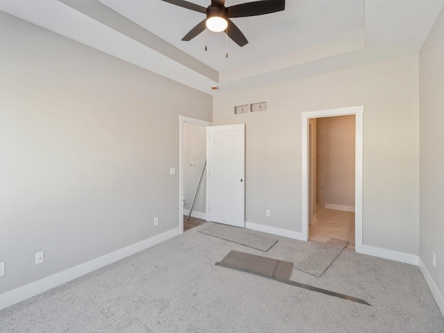 unfurnished bedroom featuring ceiling fan, a raised ceiling, and carpet floors