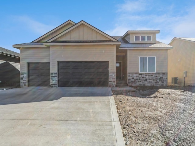 view of front facade featuring driveway, stone siding, board and batten siding, a garage, and central AC unit