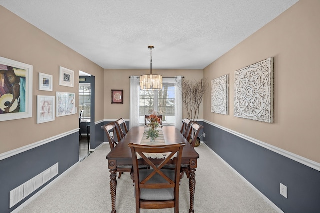 carpeted dining room featuring a textured ceiling and an inviting chandelier