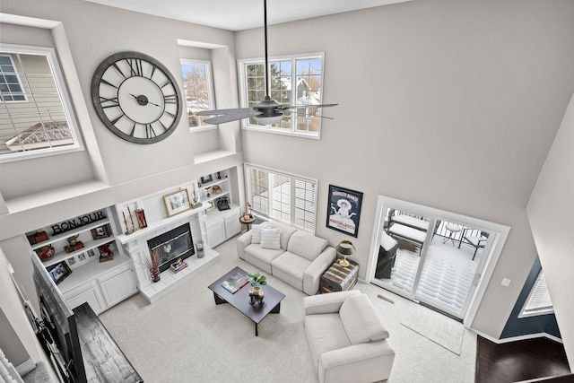 living room featuring carpet flooring, a towering ceiling, a tiled fireplace, ceiling fan, and built in features