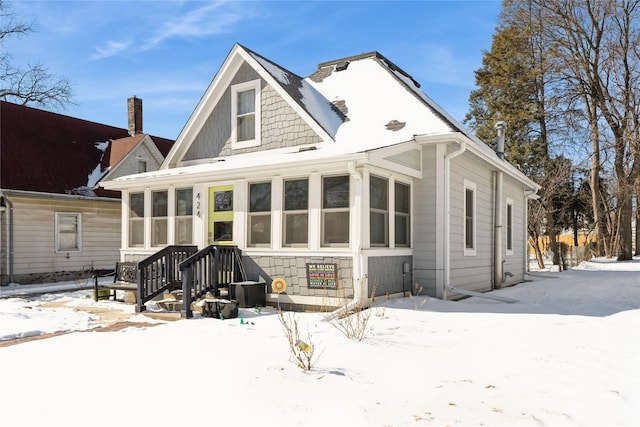 snow covered rear of property featuring a sunroom