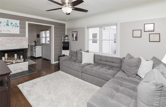 living room with ceiling fan, a tiled fireplace, and dark wood-style flooring