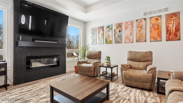 living area with a fireplace, wood finished floors, visible vents, and baseboards