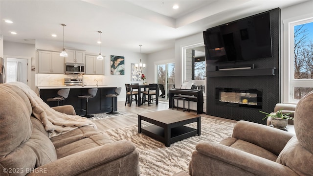 living area featuring light wood-type flooring, a large fireplace, an inviting chandelier, and recessed lighting