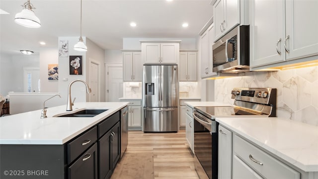 kitchen with hanging light fixtures, appliances with stainless steel finishes, a sink, and a kitchen island with sink