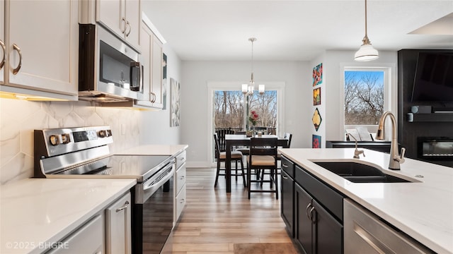 kitchen featuring white cabinets, decorative backsplash, appliances with stainless steel finishes, pendant lighting, and a sink