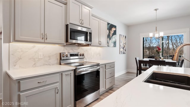 kitchen with appliances with stainless steel finishes, wood finished floors, a sink, pendant lighting, and backsplash