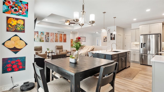 dining space featuring a tray ceiling, recessed lighting, visible vents, light wood-type flooring, and ceiling fan with notable chandelier