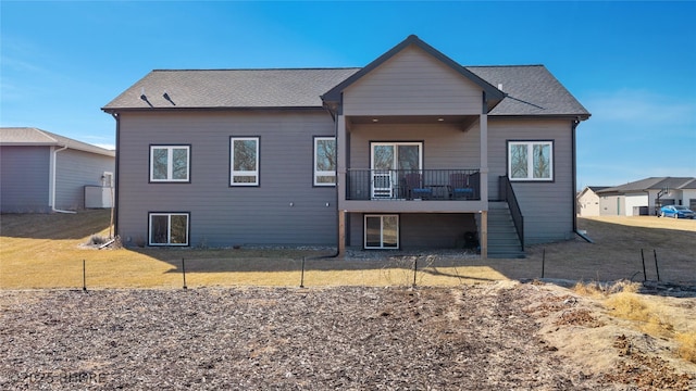 rear view of property featuring roof with shingles, a lawn, and stairway