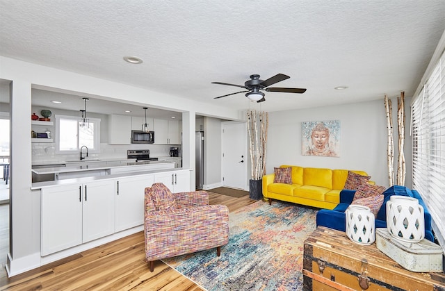 living room featuring ceiling fan, sink, light hardwood / wood-style floors, and a textured ceiling