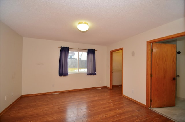 spare room featuring a textured ceiling, wood finished floors, and baseboards