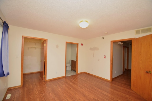 unfurnished bedroom featuring visible vents, a spacious closet, light wood-style floors, a textured ceiling, and baseboards