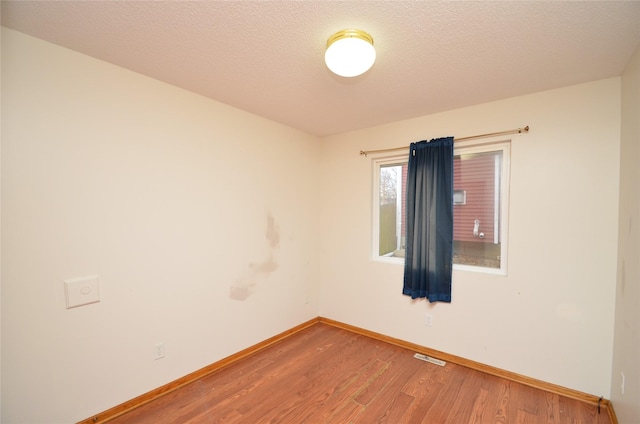 spare room featuring baseboards, a textured ceiling, visible vents, and wood finished floors