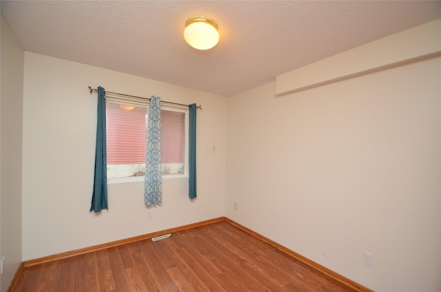 spare room with visible vents, a textured ceiling, baseboards, and wood finished floors