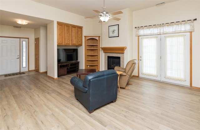 living room featuring a ceiling fan, baseboards, visible vents, a tile fireplace, and light wood-type flooring