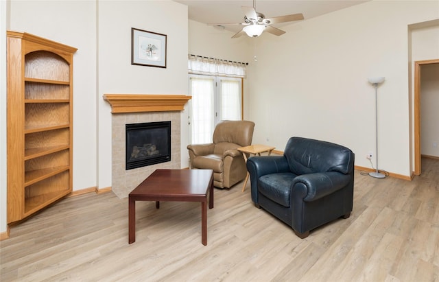 living room featuring a tiled fireplace, baseboards, light wood finished floors, and ceiling fan