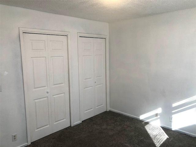 unfurnished bedroom featuring dark carpet, two closets, and a textured ceiling