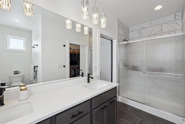 full bathroom featuring double vanity, a spacious closet, a shower stall, and a sink
