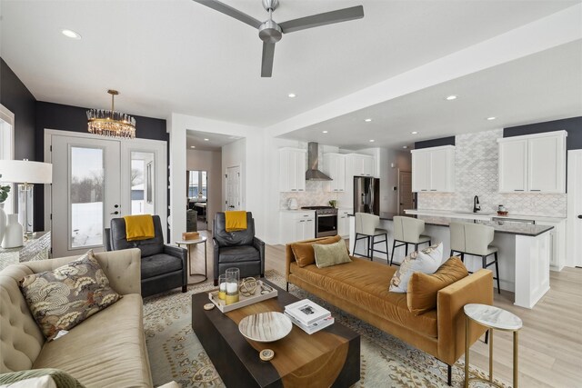 living room with recessed lighting, ceiling fan with notable chandelier, light wood-style floors, and french doors