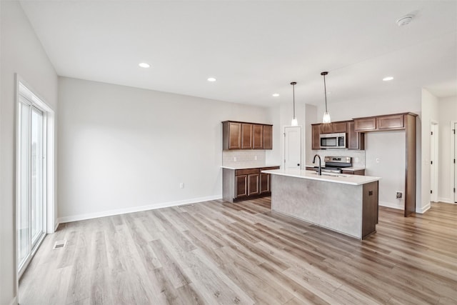 kitchen with a center island with sink, hanging light fixtures, appliances with stainless steel finishes, and light hardwood / wood-style floors