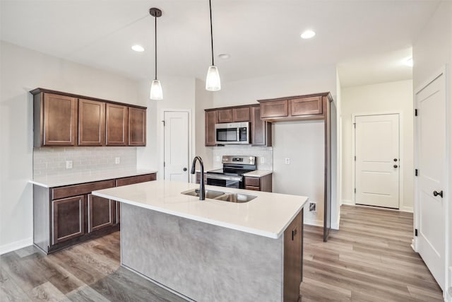 kitchen with an island with sink, appliances with stainless steel finishes, hardwood / wood-style flooring, and decorative light fixtures