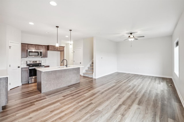 kitchen with hanging light fixtures, stainless steel appliances, an island with sink, sink, and light wood-type flooring