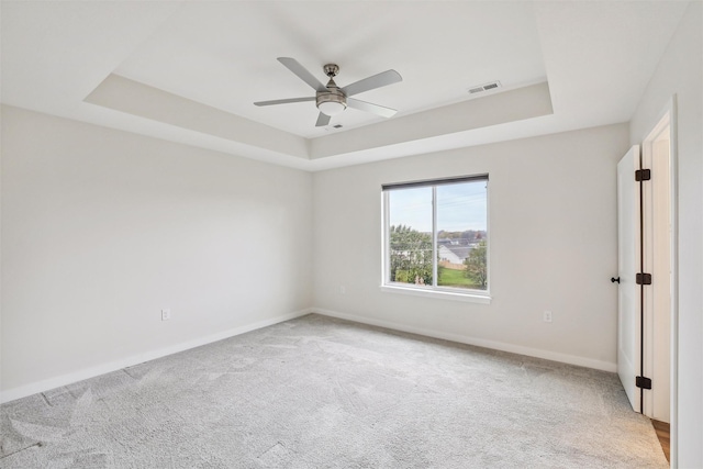 carpeted empty room with ceiling fan and a raised ceiling