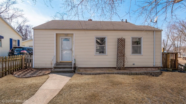 rear view of house featuring a yard, entry steps, fence, and a shingled roof