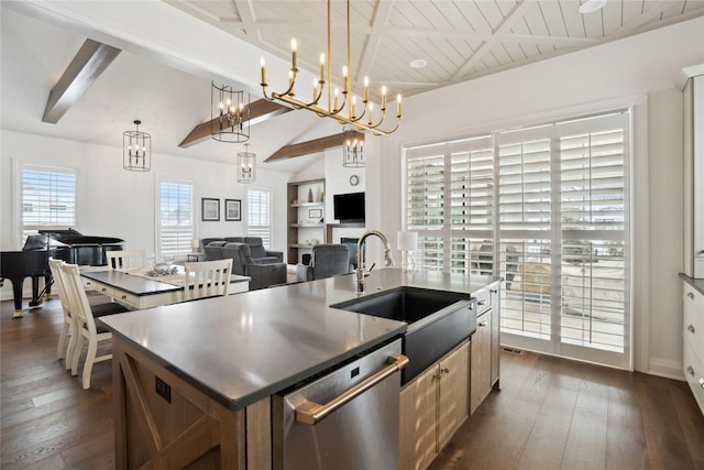 kitchen with sink, pendant lighting, lofted ceiling with beams, stainless steel dishwasher, and a kitchen island with sink