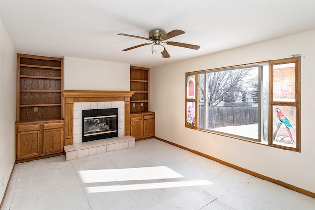 unfurnished living room with built in features, a tiled fireplace, and ceiling fan