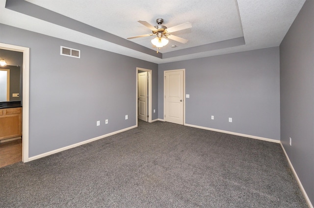 unfurnished room with a tray ceiling, ceiling fan, dark colored carpet, and a textured ceiling