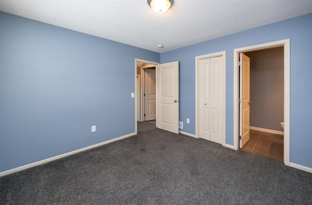 unfurnished bedroom with dark carpet, a textured ceiling, and a closet