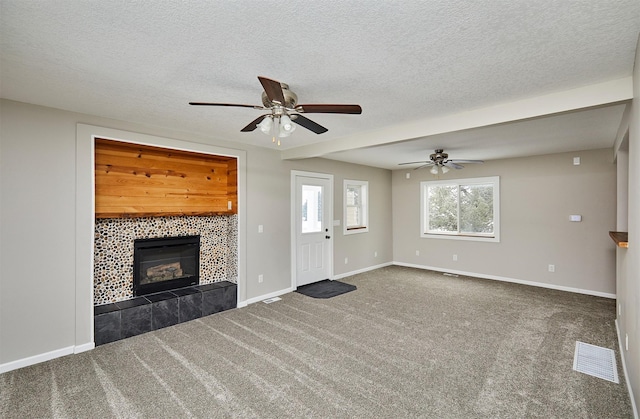 unfurnished living room featuring dark carpet, a tiled fireplace, ceiling fan, and a textured ceiling