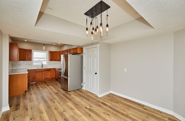 kitchen featuring stainless steel appliances, decorative light fixtures, light hardwood / wood-style floors, a tray ceiling, and sink