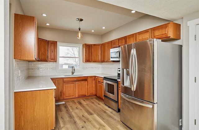 kitchen featuring tasteful backsplash, hanging light fixtures, light wood-type flooring, stainless steel appliances, and sink