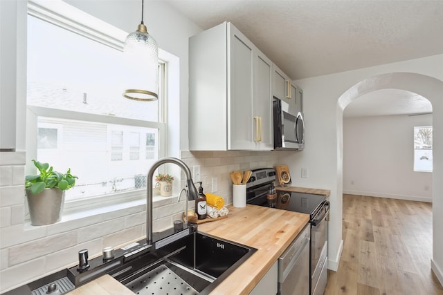 kitchen with butcher block counters, decorative light fixtures, light hardwood / wood-style floors, stainless steel appliances, and tasteful backsplash